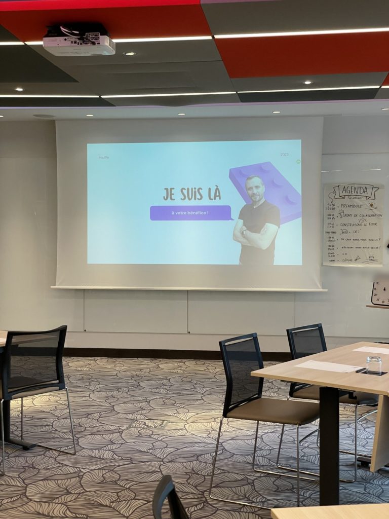 Salle prête avant l'atelier : écran « Je suis là, à votre bénéfice ! » et agenda de la journée au mur (wifi du lieu flouté)